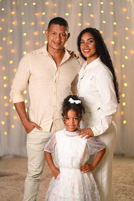 Pai, mãe e filha em roupa social diante da cortina de luzes